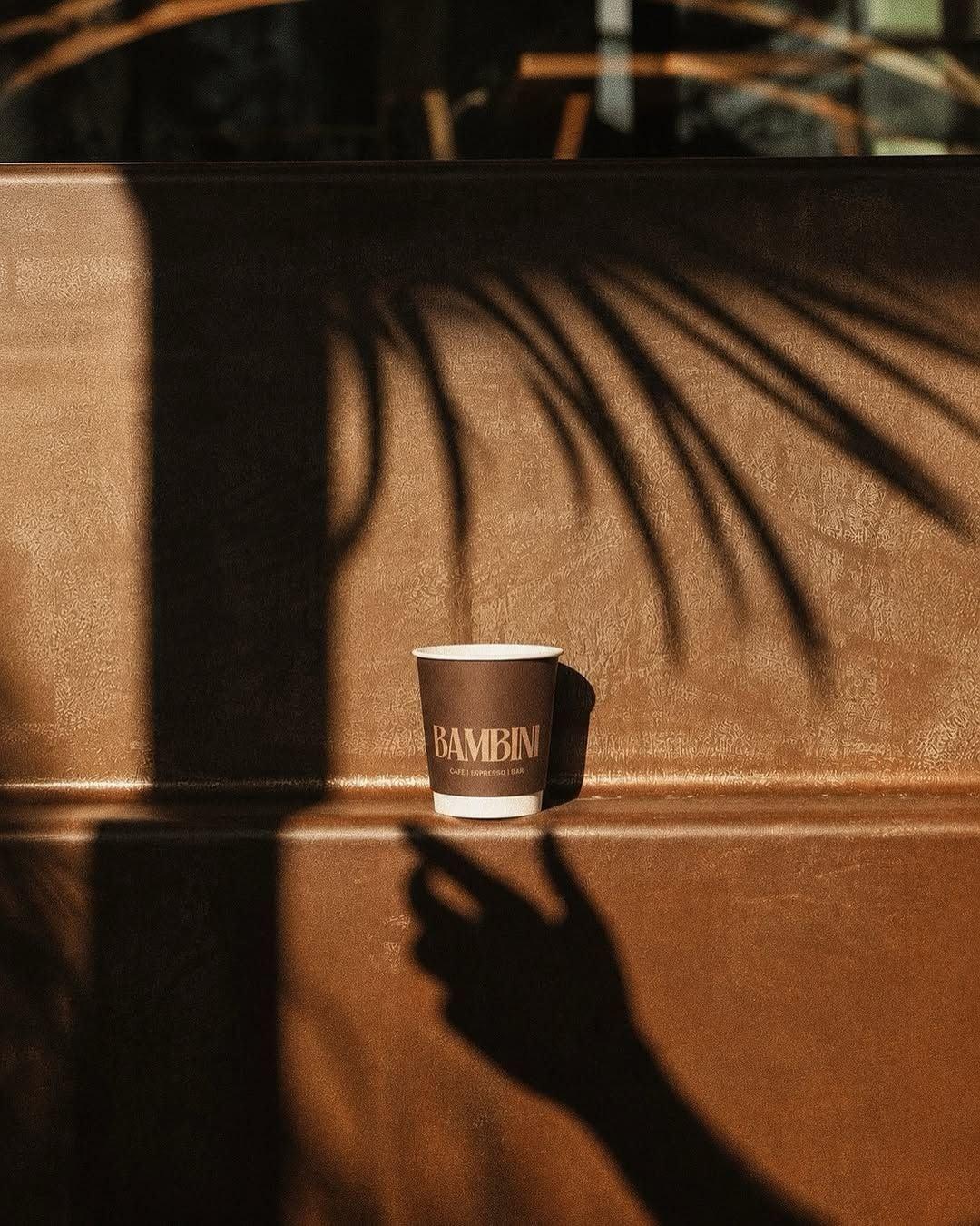 A Bambini Lombok branded takeaway coffee cup against a sunlit wall.